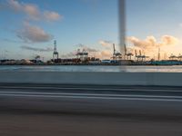 a beach with boats and cranes in the background taken from a vehicle window at dusk