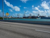 a road going by the ocean with two large ships in the background and blue sky with white clouds