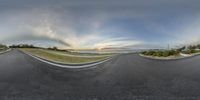 a panoramic view of an empty road in the morning sun set and the sky has clouds above it