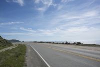 a lone motorcycle rests in the middle of a road overlooking the ocean and hills with grass