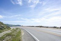 a lone motorcycle rests in the middle of a road overlooking the ocean and hills with grass