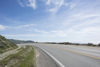 a lone motorcycle rests in the middle of a road overlooking the ocean and hills with grass