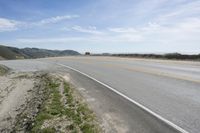 a lone motorcycle rests in the middle of a road overlooking the ocean and hills with grass