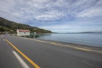 the road runs beside a body of water and there is a boat on it with a shed in the background