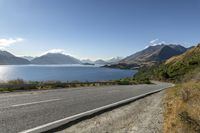 a road near the water with mountains in the background and blue sky on the far side