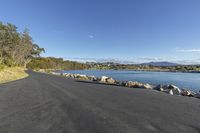 a view looking down an empty road with a lake in the distance and several trees on both sides