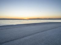 a lone man rides a skateboard down a beach at sunset on a clear day