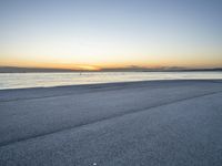 a lone man rides a skateboard down a beach at sunset on a clear day