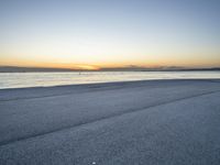 a lone man rides a skateboard down a beach at sunset on a clear day