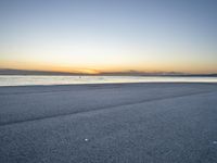 a lone man rides a skateboard down a beach at sunset on a clear day