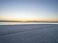 a lone man rides a skateboard down a beach at sunset on a clear day