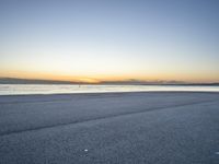 a lone man rides a skateboard down a beach at sunset on a clear day