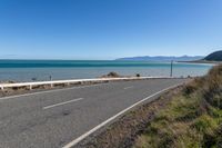 a scenic and empty road is by the sea with a white bench next to it