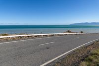 a scenic and empty road is by the sea with a white bench next to it