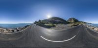 a fish - eye photo of a mountain with some water in the background and a long road on one side