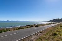 a road by the water and mountains with blue skies in the distance of it is an island on a body of water