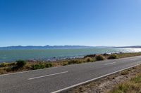 a road by the water and mountains with blue skies in the distance of it is an island on a body of water