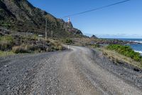 the road runs next to an area with rocks and grass and mountains behind it, and two lighthouses are on a cliff