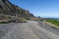 the road runs next to an area with rocks and grass and mountains behind it, and two lighthouses are on a cliff