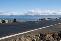 the road by the ocean has many rocks and sand on it in it, with mountains in the background