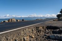 the road by the ocean has many rocks and sand on it in it, with mountains in the background