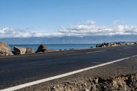 the road by the ocean has many rocks and sand on it in it, with mountains in the background