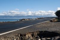 the road by the ocean has many rocks and sand on it in it, with mountains in the background