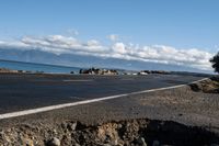 the road by the ocean has many rocks and sand on it in it, with mountains in the background