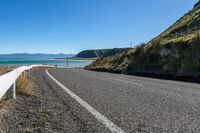 the road is empty along the beach side and its paved by the water, with hills around it