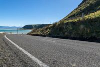 the road is empty along the beach side and its paved by the water, with hills around it