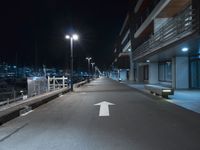 a dark, empty sidewalk lit up at night by street lights and concrete benches under large lamps