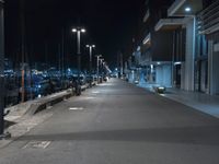 a dark, empty sidewalk lit up at night by street lights and concrete benches under large lamps