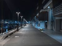 a dark, empty sidewalk lit up at night by street lights and concrete benches under large lamps