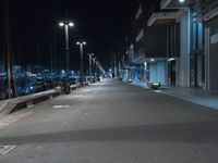 a dark, empty sidewalk lit up at night by street lights and concrete benches under large lamps