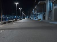 a dark, empty sidewalk lit up at night by street lights and concrete benches under large lamps