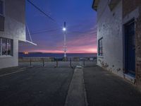 an empty road leading to some buildings and a sea at night time in the background