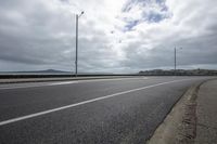 a wide asphalt road on an overcast day with clouds in the sky above it