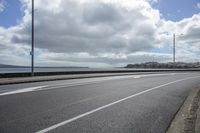 a car driving on an empty street next to the sea under a cloudy sky with a large body of water in the distance