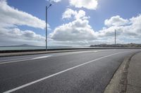 a car driving on an empty street next to the sea under a cloudy sky with a large body of water in the distance