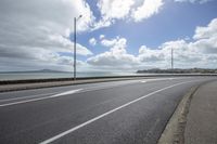 a car driving on an empty street next to the sea under a cloudy sky with a large body of water in the distance