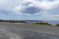 a empty road, with mountains in the distance and an ocean below it as seen from a pointy viewpoint