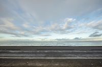 a wide shot of a road next to the ocean and sky with some clouds on it