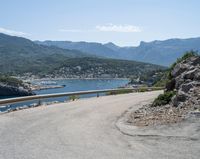 a view looking down at a large body of water from a curved road near the side of a mountain