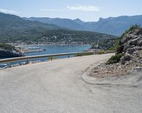 a view looking down at a large body of water from a curved road near the side of a mountain