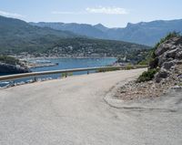 a view looking down at a large body of water from a curved road near the side of a mountain