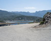 a view looking down at a large body of water from a curved road near the side of a mountain