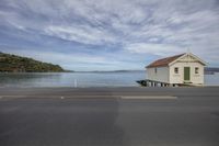 a small white house sits next to the water in a parking lot in front of a boat