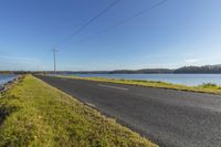 a scenic road beside a lake with power lines above it on the edge of a grassy field