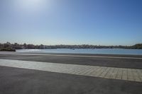 an empty paved surface overlooking water and some buildings and trees to the side of it