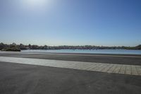 an empty paved surface overlooking water and some buildings and trees to the side of it